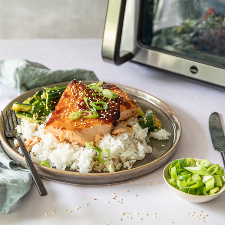 A modern black and stainless steel DUALFRY GRILL 10L air fryer with dual heating elements and a digital control panel on top. Inside the glass door, food is visible being cooked. The display shows the temperature as 200°C and the time remaining as 18 minutes. A truly powerful air fryer.