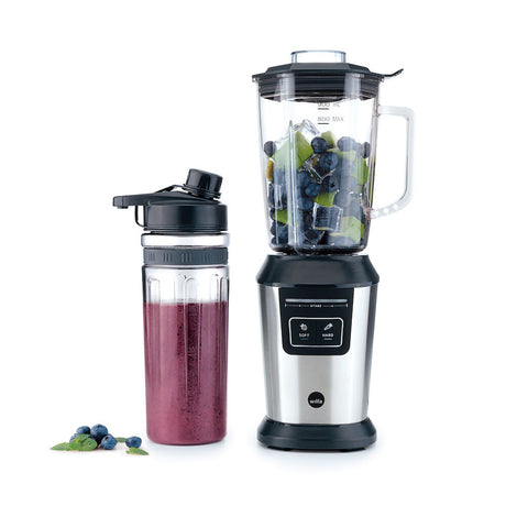 A stainless steel sports blender with a transparent pitcher filled with blueberries, spinach, and other fruits. Next to it is an ACTIVLIFE STEEL 2go bottle containing a dark purple smoothie topped with a secure lid. A small bunch of blueberries and a couple of mint leaves are placed nearby.