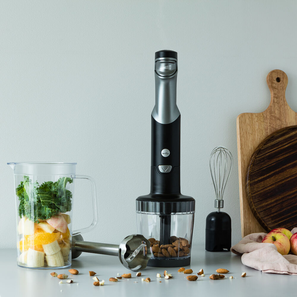 A black and silver ESSENTIAL POWER set with a powerful motor and stepless speed control, featuring three components: the blender handle, a clear measuring pitcher filled with chopped red onions, and a clear food processor attachment containing chopped vegetables, including red onions and green peppers.